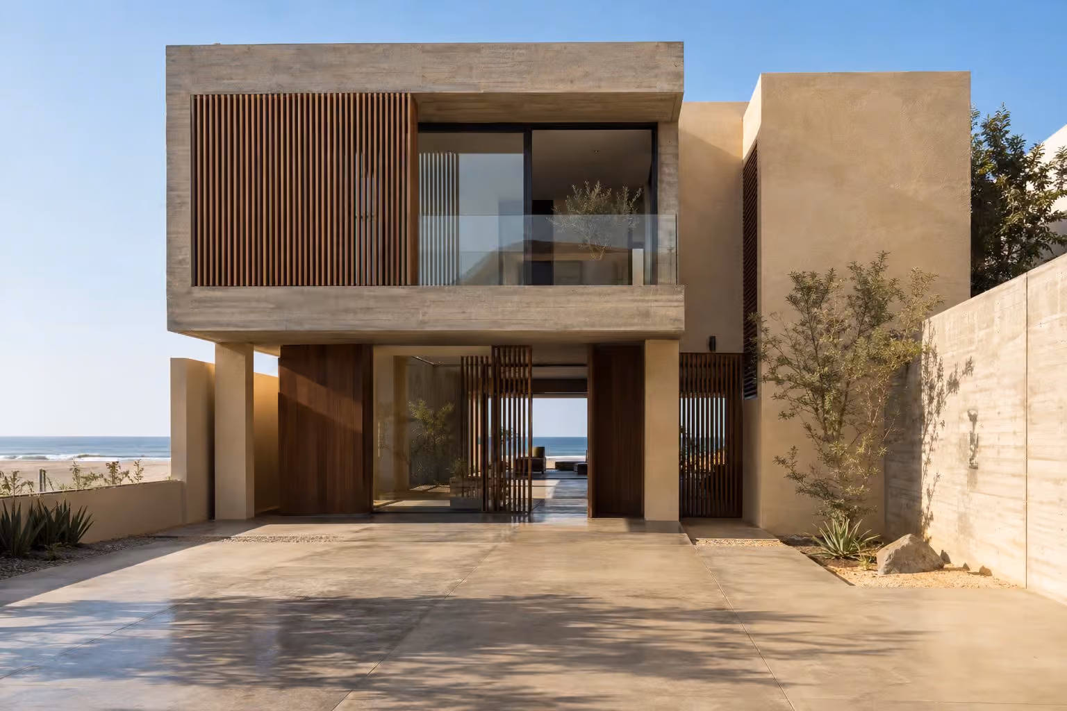 Casa de dos pisos de concreto caravista y celosías de madera frente al mar